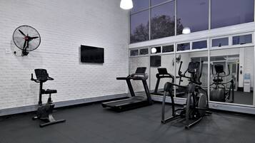 A gym with exercise equipment, a large mirror, and a white brick wall.
