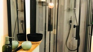 Une salle de bain moderne avec une douche à l’italienne en verre, un meuble-lavabo en bois avec des vasques noires et vertes, et un miroir.