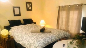 Une chambre à coucher avec un lit, une table de chevet, une lampe et une petite table ronde sur laquelle est posée une plante.