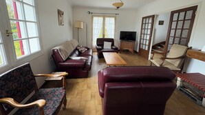 Una sala de estar con un sofá, sillas, un televisor y una mesa de centro de madera.