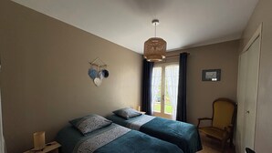 Un dormitorio con dos camas, una lámpara colgante, una silla y una ventana con cortinas.