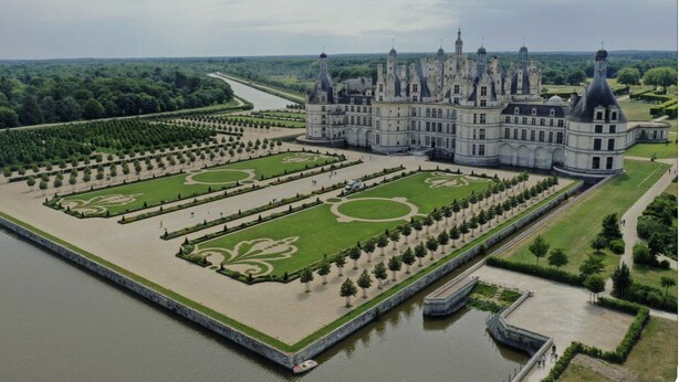 Un gran castillo con jardines simétricos, un río y un foso.