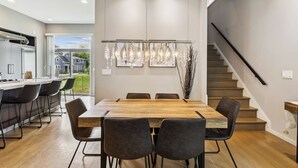 A modern kitchen with a large island, a dining area with a wooden table and chairs, and a staircase leading to an upper level.