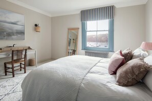Une chambre avec un grand lit, un bureau, une chaise, une fenêtre donnant sur les bateaux et un radiateur.