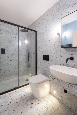 Une salle de bain moderne avec une douche à parois de verre, des toilettes blanches et un lavabo blanc doté d’un robinet noir.
