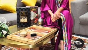 A room with a sofa, a coffee table with a board game, and a wooden door with a colorful sign. - Riad Luxe Location LE Grizzly - Chambre LA Kasbah (Marrakech)