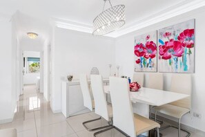 A bright dining area with white furniture, a chandelier, and floral artwork on the wall. - CristiSmart Home, Hi-End Services, Media Streaming (Los Cristianos)