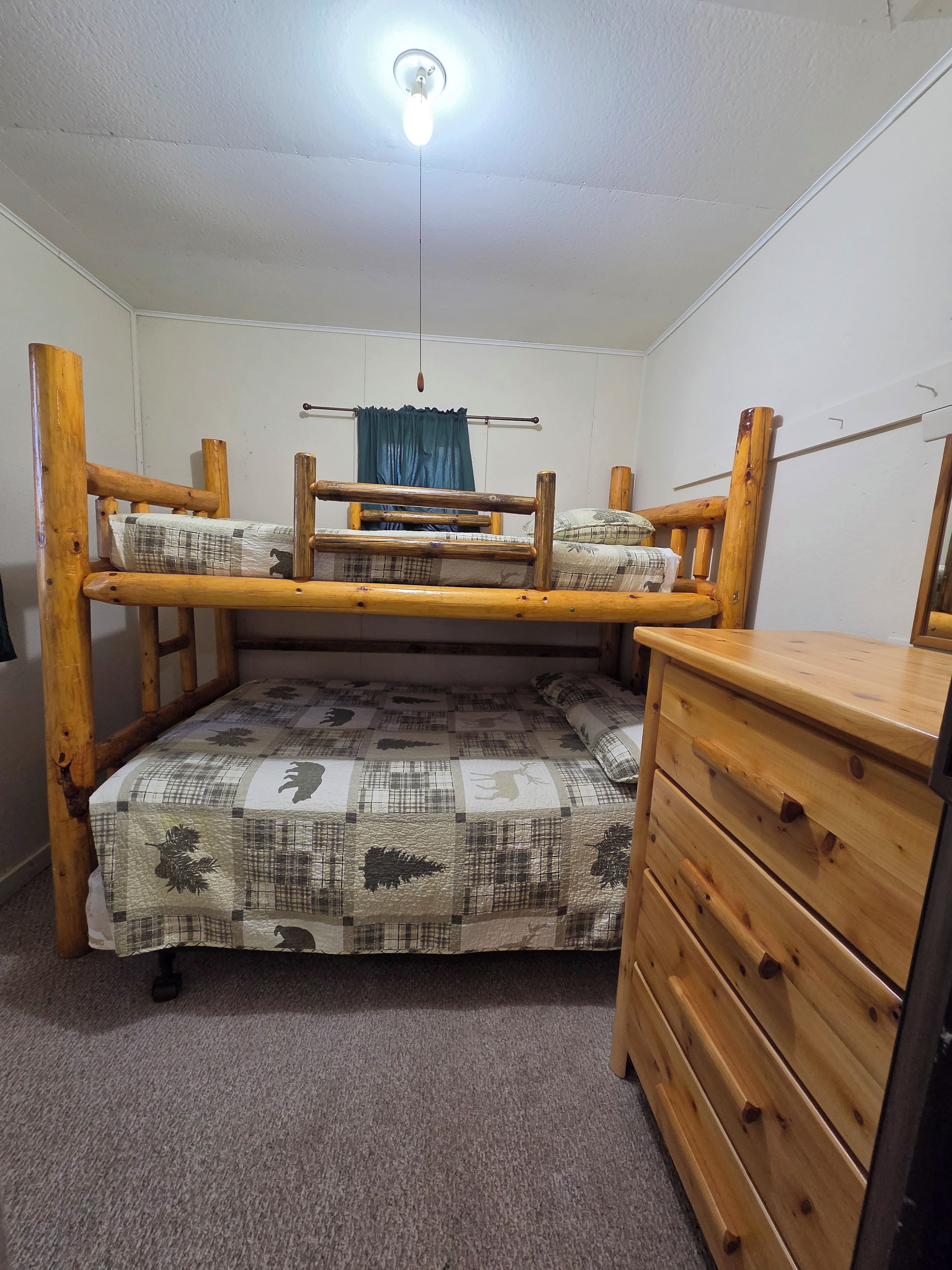 A bunk bed with a wooden frame, a quilted mattress, and a wooden dresser with drawers.