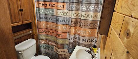 A cabin-style bathroom with a shower curtain featuring cabin rules, a toilet, a sink, and wooden walls.
