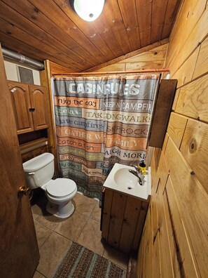 Een badkamer in chaletstijl met douchegordijn waarop regels staan, een toilet, een wastafel en houten wanden.