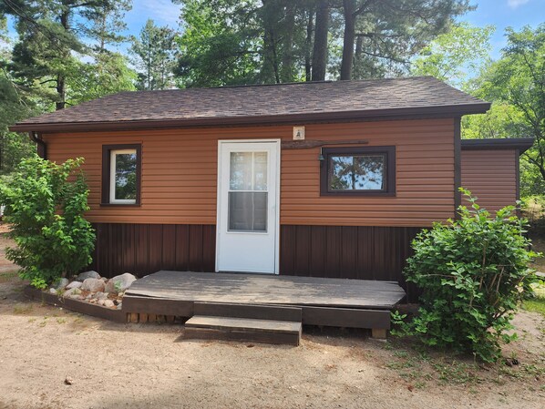 A small wooden cabin with a white door, two windows, and a front porch.
