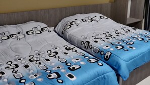 Une chambre d’hôtel avec deux lits, chacun agrémenté de draps à motifs et dotée d’un ventilateur de plafond.