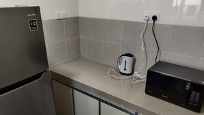 Une cuisine équipée d’un réfrigérateur en acier inoxydable, d’une bouilloire électrique blanche et d’un four à micro-ondes noir, le tout posé sur un plan de travail carrelé.