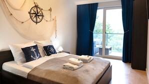 Habitación de hotel con cama, un ventanal con cortinas, vistas al exterior, un adorno en la pared y una cama bien tendida con toallas.