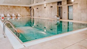 Una piscina con fondo de cristal transparente, rodeada de sillones de descanso y suelo de baldosas.
