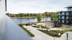Un parque junto al río con un área de juegos, bancos y un edificio moderno con ventanas de vidrio.