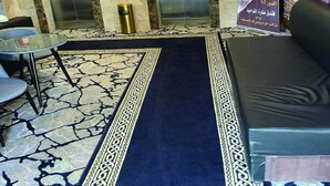 An elevator area with two elevators, a small table with a chair, a blue carpet, and a sofa. - Askant Al Hafayer (Makkah)