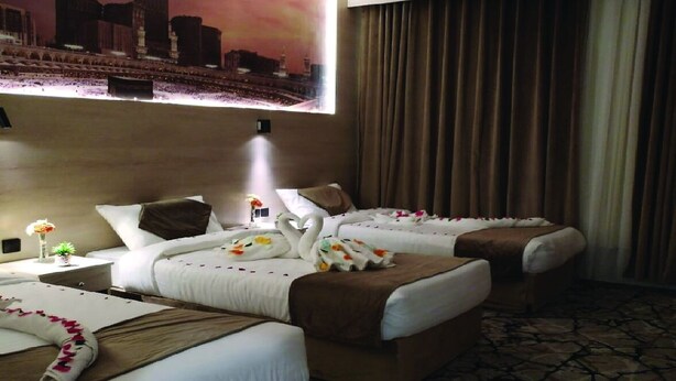 A hotel room with two beds, a large cityscape painting on the wall, and a view of the city. - Askant Al Hafayer (Makkah)