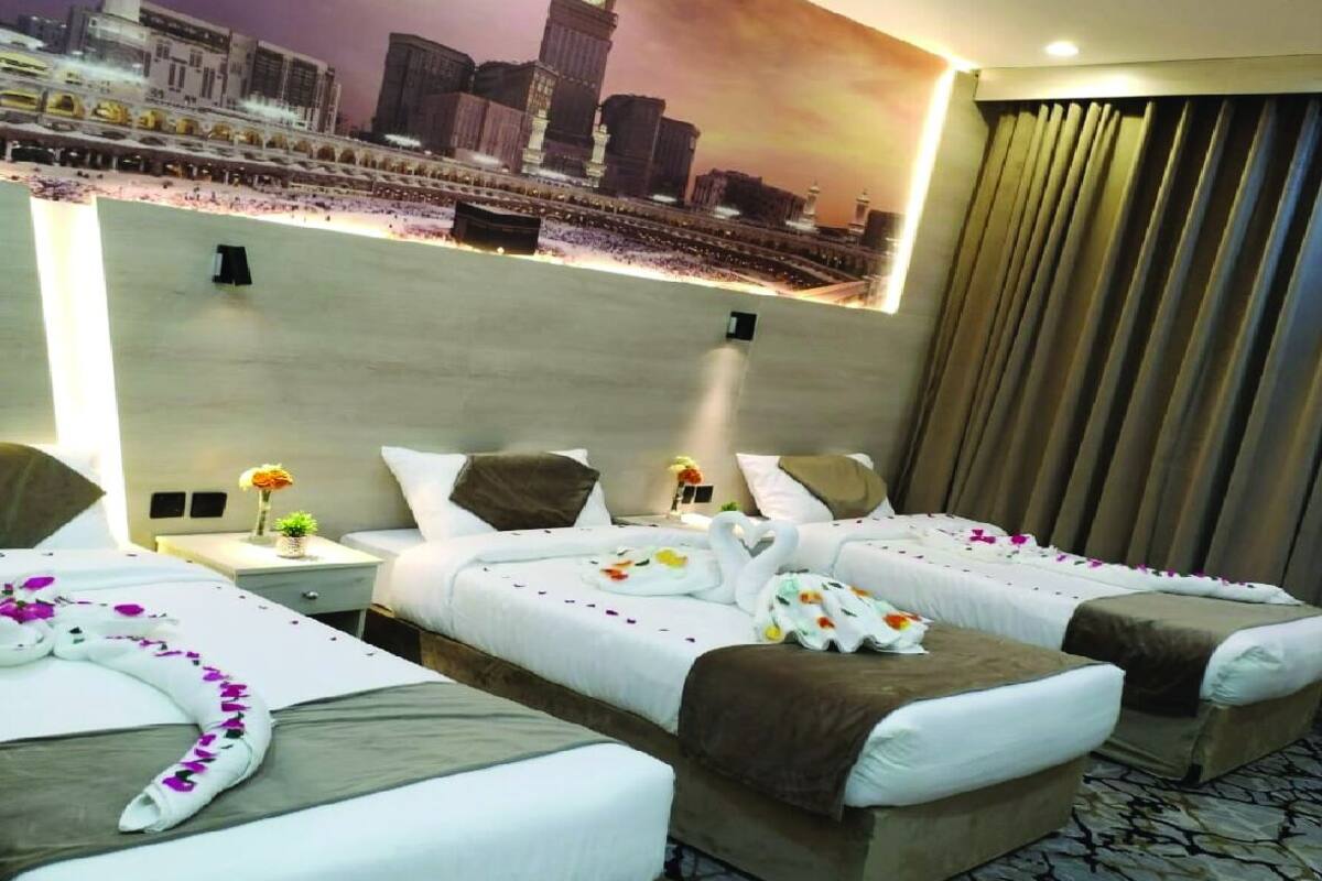 A hotel room with two beds, a nightstand with a vase of flowers, and a large cityscape mural on the wall.