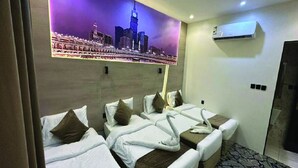A hotel room with four beds arranged in a row, a cityscape mural on the wall, an air conditioning unit, and a patterned floor. - Askant Al Hafayer (Makkah)