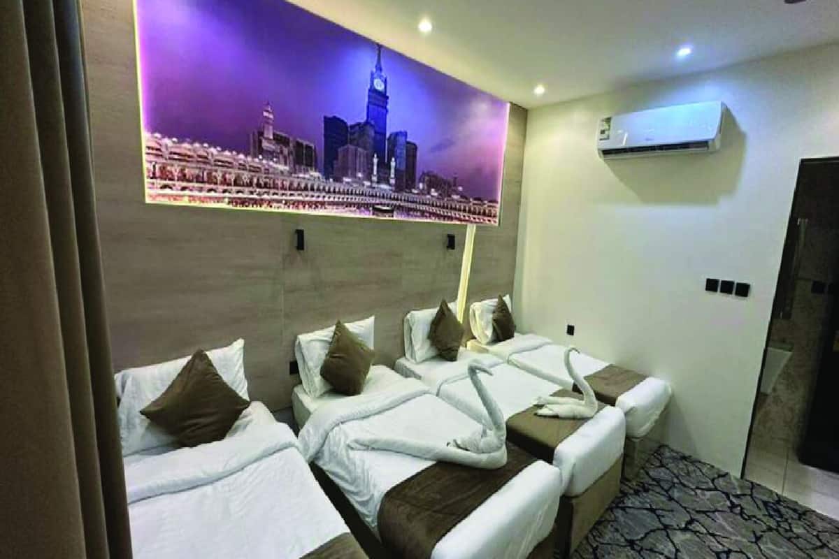 A hotel room with four beds arranged in a row, a cityscape mural on the wall, an air conditioning unit, and a patterned floor.