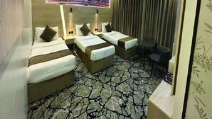 A hotel room with three beds, a cityscape mural, a patterned floor, and a small table with chairs. - Askant Al Hafayer (Makkah)