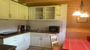 Een kleine keuken met witte kastjes, een magnetron en een houten tafel met een rood tafelkleed.