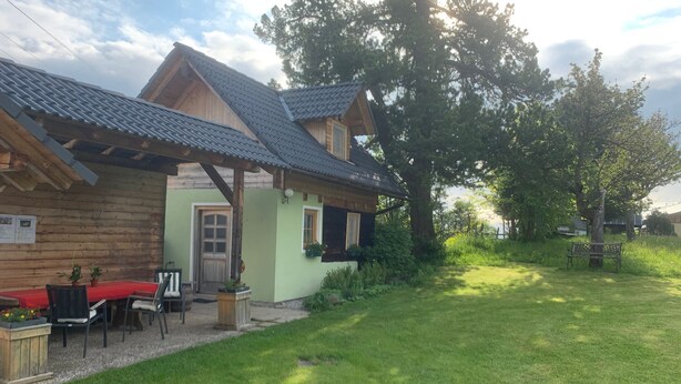 Een houten huis met een schuin dak, een veranda met een bankje en een gazon.