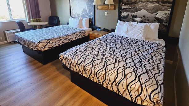 A hotel room with two beds, a desk, a chair, a lamp, and a painting of mountains. - Wyo Inn  (Sheridan)