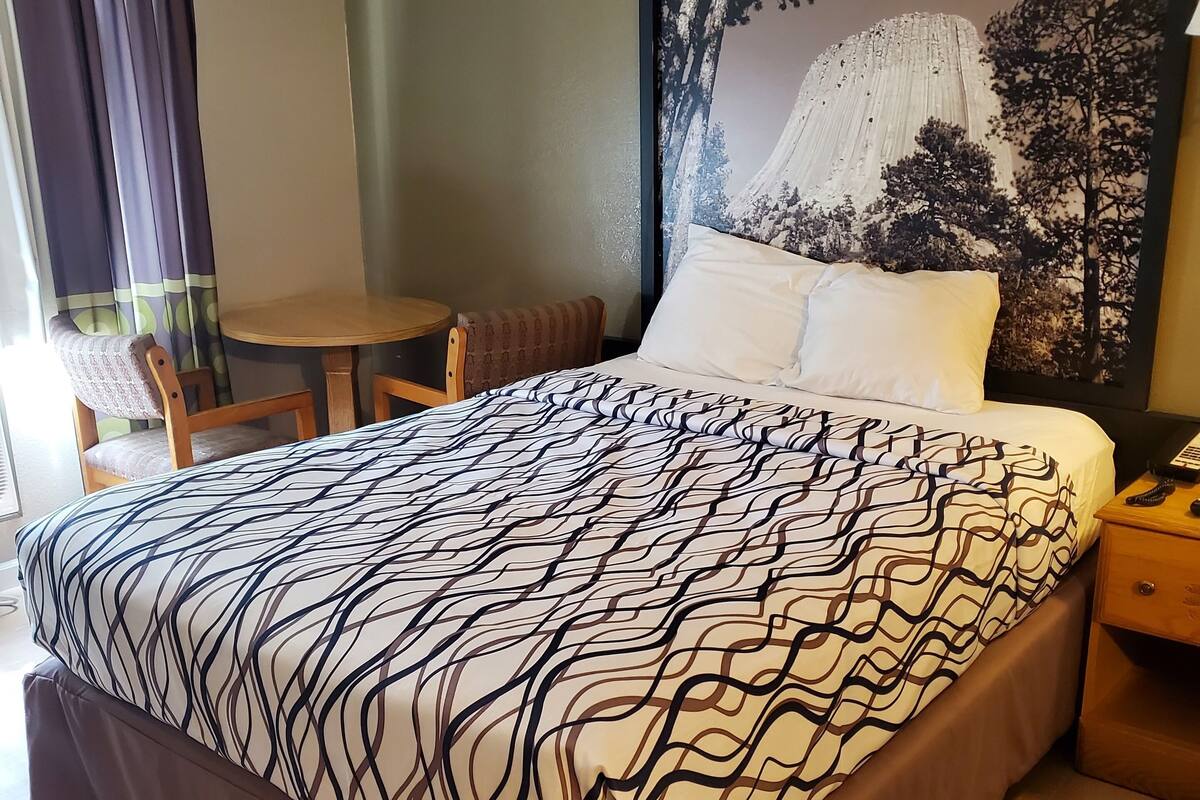 Une chambre avec un grand lit, une table de chevet en bois, une chaise, une petite table et une grande fresque murale.