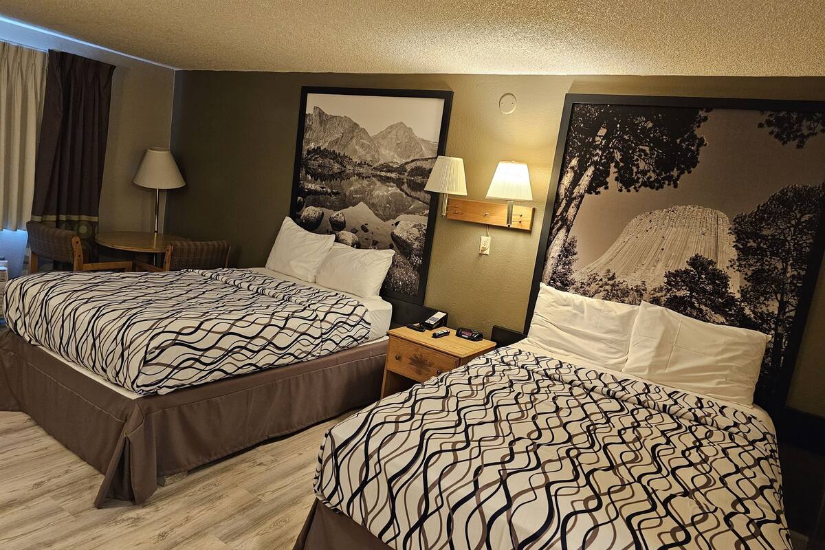 Une chambre d’hôtel avec deux lits, une petite table, une chaise et une lampe fixée au mur.