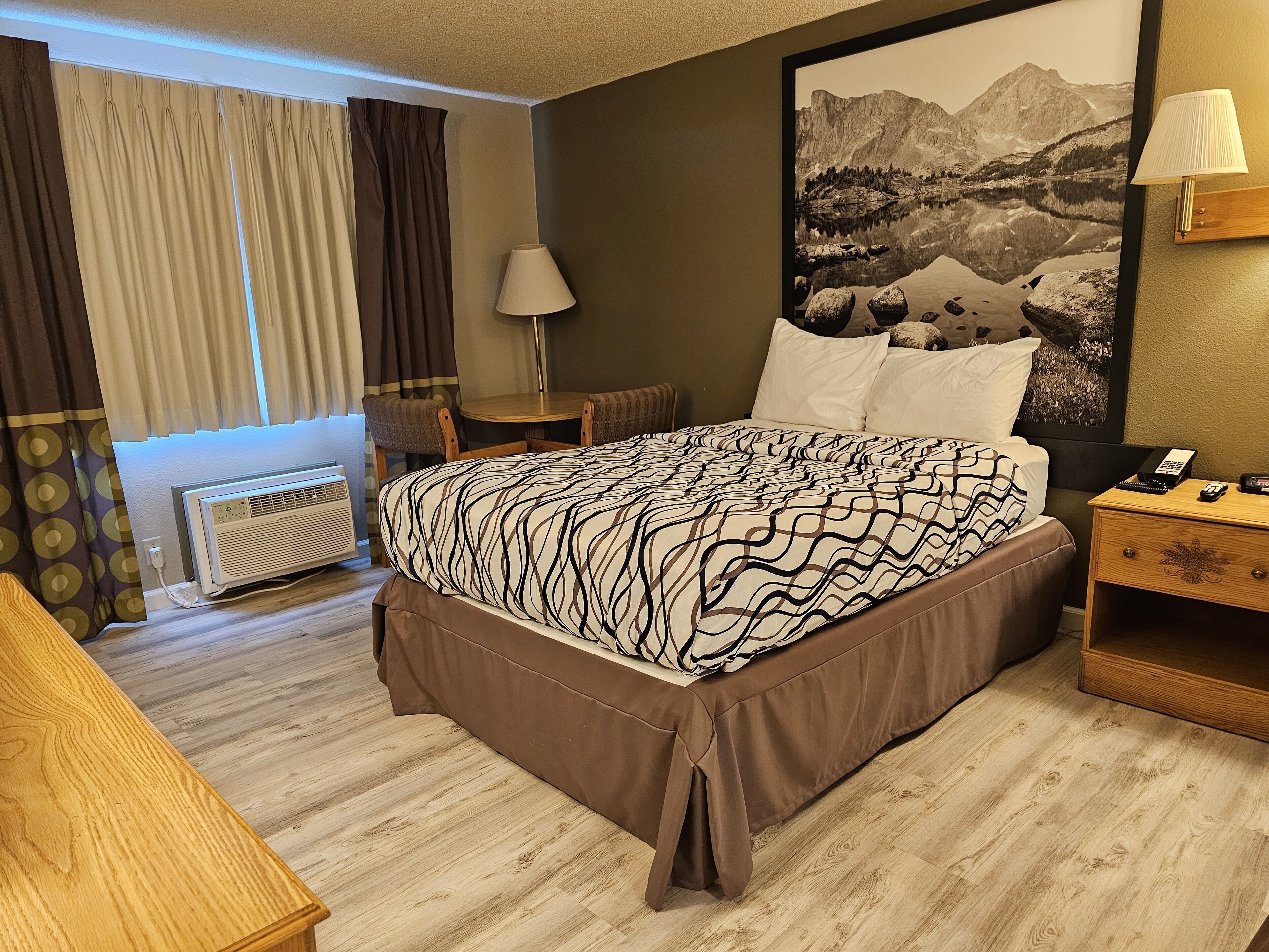 A hotel room with a large bed, a desk, a chair, a lamp, and a painting on the wall.