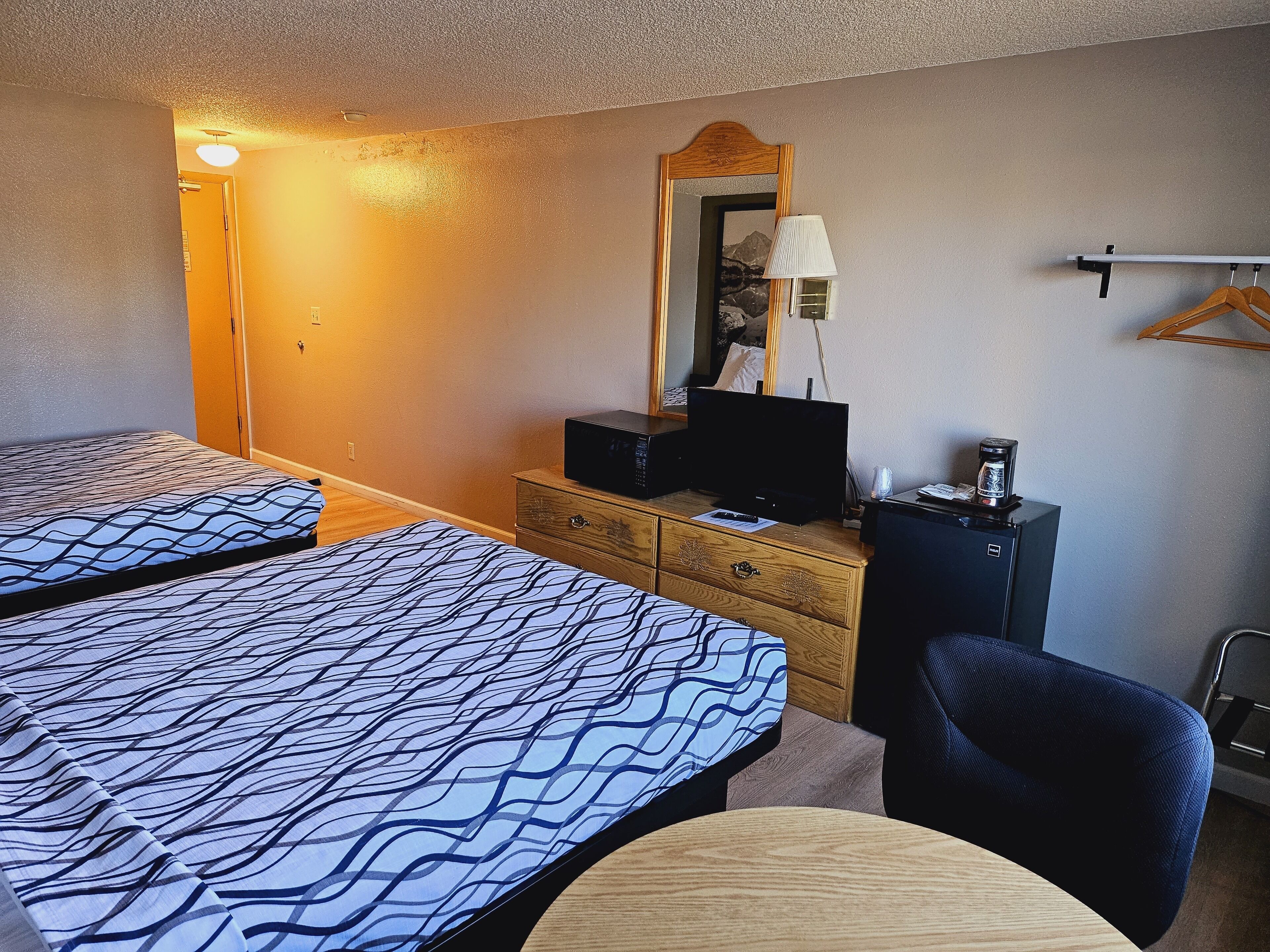 A hotel room with two beds, a desk, a chair, a television, and a coffee maker.