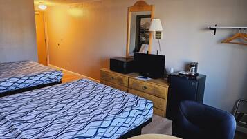 A hotel room with two beds, a desk, a chair, a television, and a coffee maker.