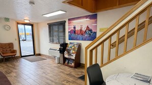 A lobby with wooden flooring, a reception desk, a black chair, a white table, and a staircase. - Wyo Inn  (Sheridan)