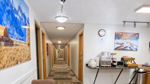 A hotel corridor with a dining area featuring a round table and chairs, a kitchen area with a coffee machine, and a mural on the wall. - Wyo Inn  (Sheridan)