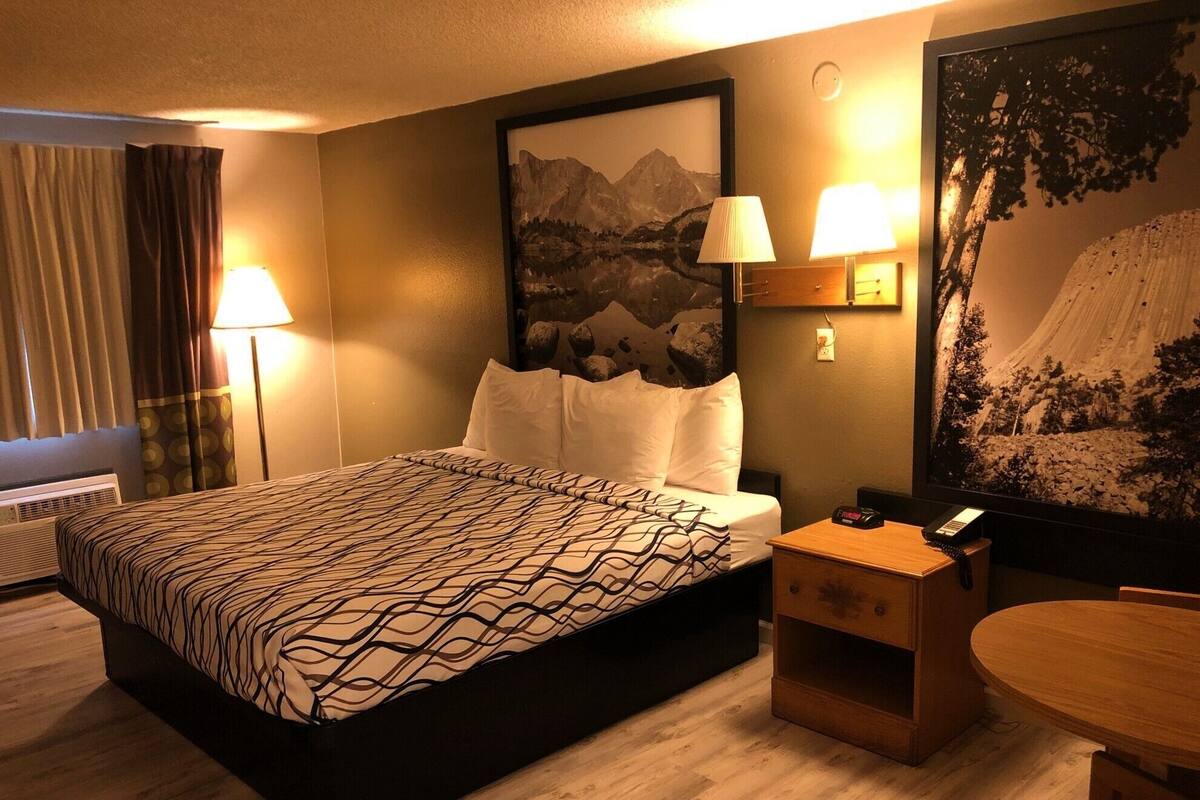 Une chambre d’hôtel avec un grand lit, deux lampes de chevet, une table de chevet, une petite table et un grand tableau encadré au mur.