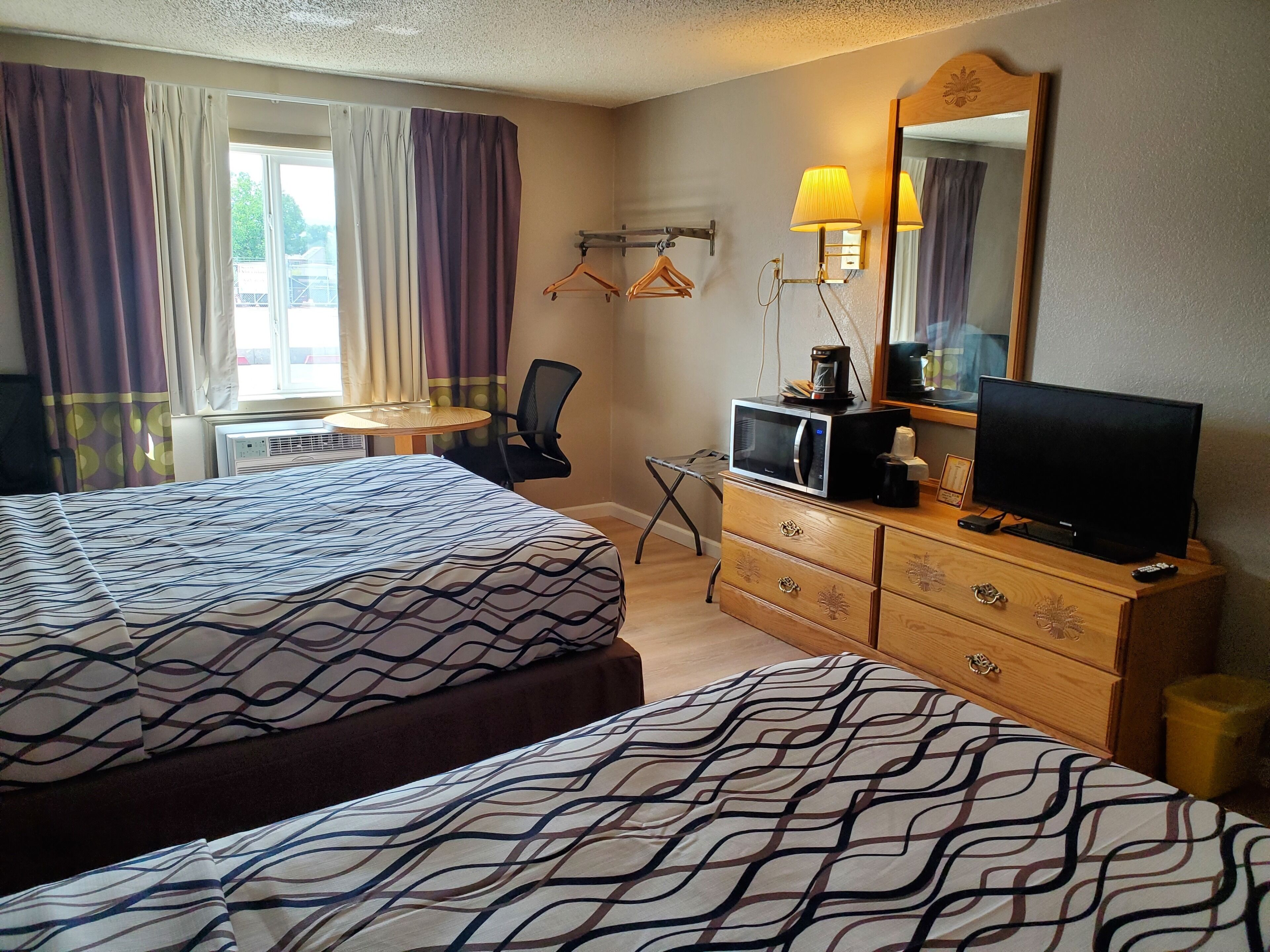 A hotel room with two beds, a desk, a chair, a television, a dresser, and a mirror.