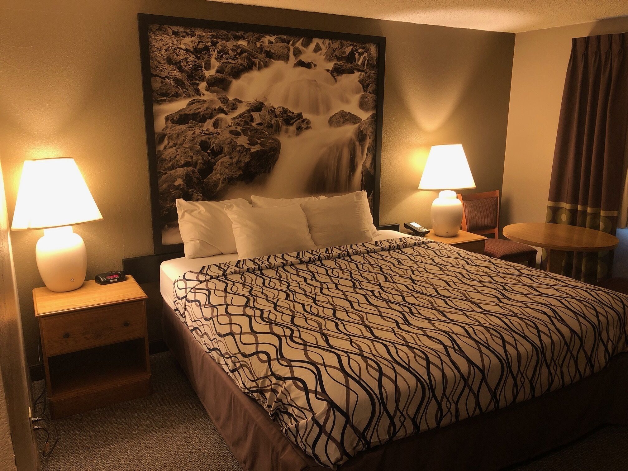Una habitació d'hotel amb un llit gran, dues làmpades de nit, una tocador, una taula petita i un quadre d'una cascada a la paret.