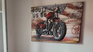 Een kamer met een gedekte tafel voor twee personen, twee rode stoelen, een schilderij van een motorfiets aan de muur, en een raam.