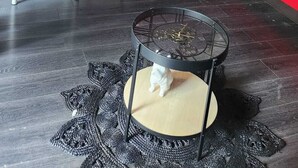 Een kleine keuken met rode kastjes, een eettafel met stoelen, een waterdispenser en een decoratief katbeeldje op een kruk.