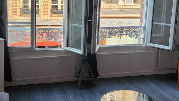 Een kamer met grote ramen, een ronde tafel en een zwart tapijt.