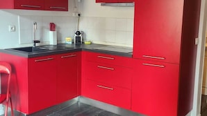 Een moderne keuken met rode kastjes, een zwart aanrecht en een ronde glazen tafel met een beeldje van een witte kat.
