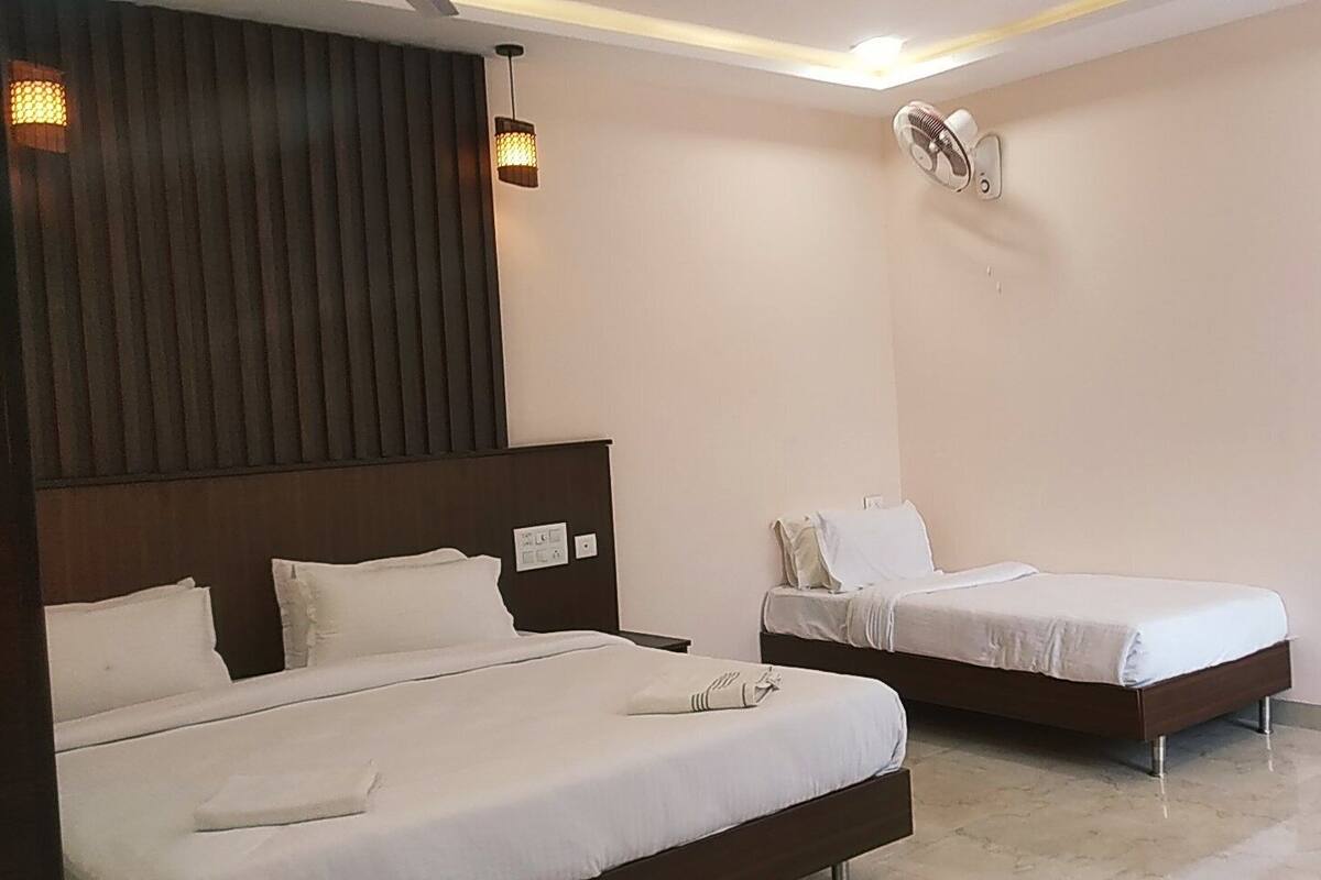 Habitación de hotel con dos camas, ventilador de techo e iluminación montada en la pared.