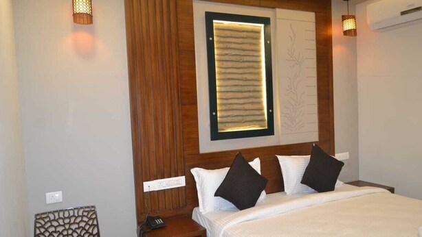 A hotel room with a bed, a nightstand, a wall-mounted lamp, and a decorative panel. - AABIL PALACE BUSINESS HOTEL (Chennai)