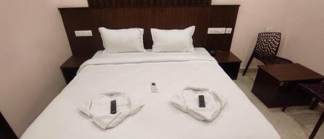 A neatly made bed with two pillows, a bedside table with a remote control, and a chair with a patterned backrest.