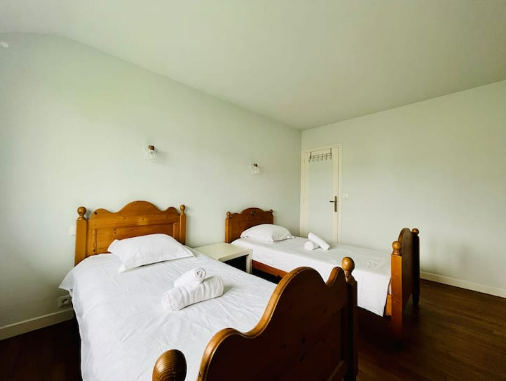 A room with two wooden beds, white linens, and a door with a towel on it.