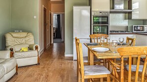 A dining area with a wooden table set for two, a sofa, and a kitchen with appliances. - 3 bedroom accommodation in Poole (Poole)