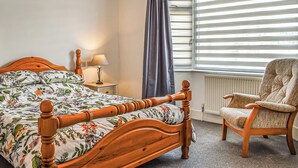 A bedroom with a wooden bed, a nightstand with a lamp, a chair, and a window with blinds. - 3 bedroom accommodation in Poole (Poole)