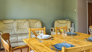 A dining area with a wooden table set for four, two cushioned chairs, and a sofa. - 3 bedroom accommodation in Poole (Poole)
